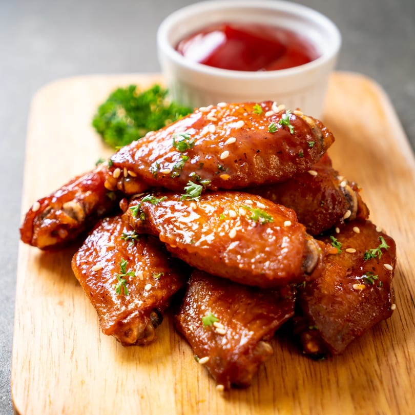Glazed BBQ chicken wings with sesame seeds and parsley, served with a side of ketchup.