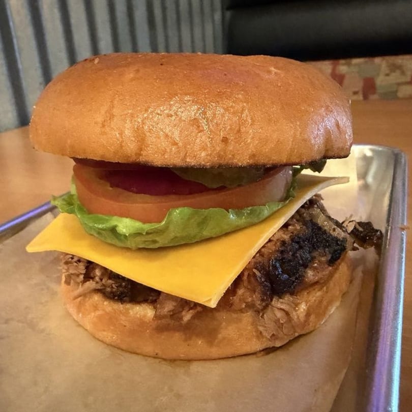 A Barbecue Nation pulled pork sandwich with cheese, lettuce, tomato, and pickles on a bun.