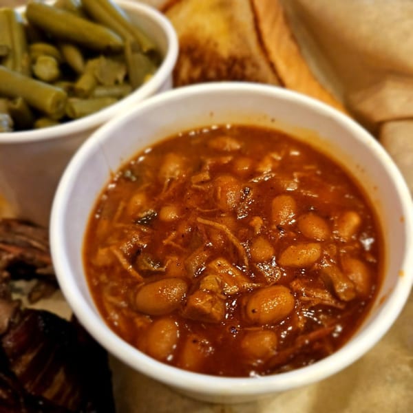 Close-up of a bowl of Barbecue Nation baked beans with green beans and toast in the background.